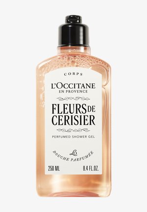 Bouteille en plastique transparent avec pompe noire. Contient un gel douche de couleur pêche. L'étiquette présente un texte noir et des éléments de design floral. 250 ML.