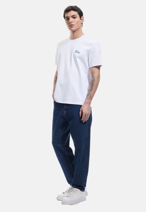 Hvid bomulds t-shirt med lyseblå logo, parret med løstsiddende mørkeblå jeans og hvide sneakers, med et afslappet design.