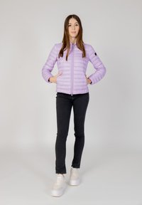 Hellblaues Puffermantel mit Stehkragen, Reißverschluss und zwei seitlichen Taschen, getragen mit schwarzen Skinny-Jeans und weißen Plateausneakern.