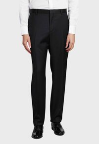 Pantaloni neri su misura realizzati in tessuto liscio, con un design a gamba dritta e tasche anteriori, abbinati a scarpe eleganti nere lucide.