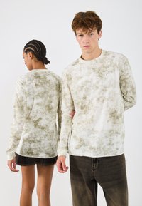 Koszula z długim rękawem w odcieniach zieleni i beżu, wykonana z miękkiego materiału. Posiada okrągły dekolt i mały detal z logo na klatce piersiowej.