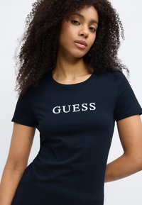 Donkerblauw T-shirt met korte mouwen, gemaakt van zachte katoen, met een ronde hals en een witte "GUESS"-logo prominent afgedrukt op de voorkant.