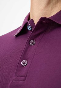 Paarse polo met een gekraagde halslijn, voorzien van drie knopen in verschillende tinten blauw. Gebreide stof met subtiele stikseldetails.