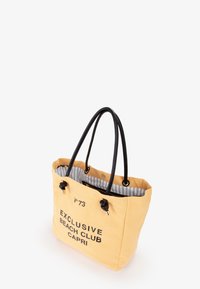Borsa a tracolla gialla con manici neri, caratterizzata da un interno a righe e la scritta stampata "EXCLUSIVE BEACH CLUB CAPRI." I manici sono annodati.