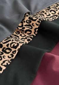 Warstwy materiału w odcieniach szarości, czerni, wzorze w panterkę i burgundzie. Miękka tekstura z miksu jednolitych kolorów i detali zwierzęcego wzoru.