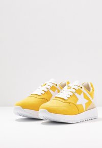 Baskets en daim jaune avec semelles en caoutchouc blanches, présentant un motif d'étoile blanche proéminente, bout rond et lacets plats.