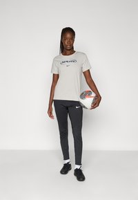 Heled hall särk sinise "SPURS" logoga ja Nike'i nööbiga; mustad sobitatud püksid tekstuuriga mustriga; hoiab musta ja valget jalgpalli.