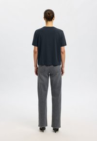 Tamsiai pilka medvilninė trumpomis rankovėmis marškinėlė, laisvo kirpimo, derinama su aukšta liemena ir tiesiomis kojomis džinsais. Kulniukai pabrėžia aprangą.