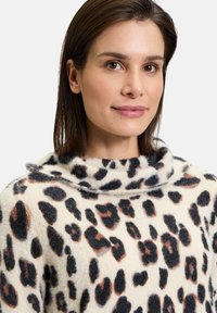 Pullover mit Kragen in einem weichen, strukturierten Stoff, der ein Leopardenmuster in Schwarz- und Brauntönen auf einem cremefarbenen Hintergrund zeigt.