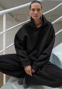 Felpa nera oversize con cappuccio e pantaloni abbinati realizzati in tessuto morbido, con una grande tasca frontale e una silhouette rilassata, abbinati a scarpe grey.