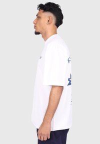 T-shirt blanc à manches courtes avec une coupe décontractée, arborant des motifs graphiques bleus sur le devant et le dos, fabriqué en coton doux.