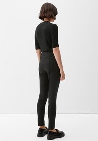Zwart aansluitend jumpsuit met driekwart mouwen, hoge taille en taps toelopende benen. Het materiaal lijkt soepel en iets rekbaar.