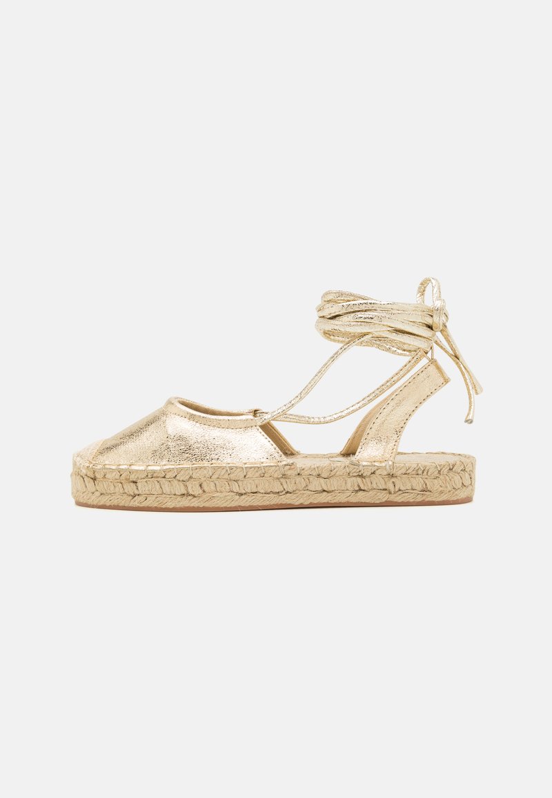 Kultaiset metalliset espadrillot, joissa on tekstuuripinta, kangasnauhavyöt ja punottu juuttipohja. Avoin varvasdesign ja tasapohja.