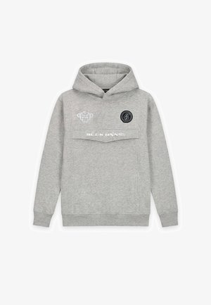 Graues Kapuzen-Sweatshirt mit einer Fronttasche, kombiniert mit hellblauen, abgenutzten Jeans mit Farbspritzern und weißen Sneakers.