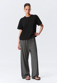 Juodas trumpomis rankovėmis marškinėliai derinami su laisvo kirpimo juodai baltai dryžuotomis kelnėmis. Aprangą papildo plokšti sandalai.