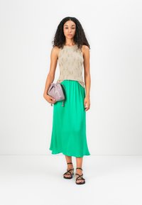 Top din tricot bej, cu un design texturat, asortat cu o fustă midi verde solidă, fluidă. Ține în mână o geantă cu sfoară de un violet deschis, purtând sandale negre.