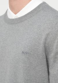 Ανοιχτό γκρι πουλόβερ με στρογγυλή λαιμόκοψη και ριμπ τελειώματα. Κεντημένο λογότυπο "BOSS" σε πιο σκούρο γκρι στην αριστερή πλευρά του στήθους.