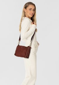 Borsa a mano in pelle marrone con una finitura texturizzata, forma rettangolare, dettagli in oro con borchie lungo i bordi e una tracolla regolabile.