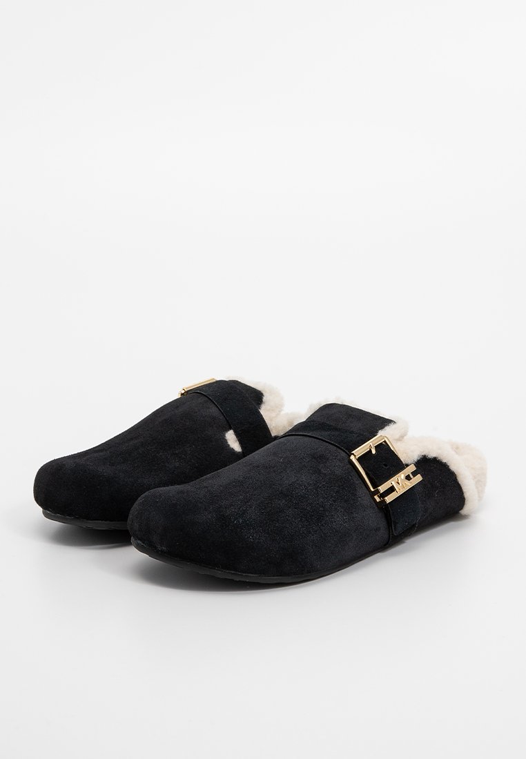 Sabots en daim noir avec une doublure crémeuse pelucheuse, dotés d'une accents en boucle dorée et d'un design à bout arrondi. Semelle plate.