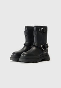 Botas de cuero negras hasta el tobillo con suela gruesa, detalles de hebilla y logo grabado en el lateral. Presentan una textura suave y punta redondeada.