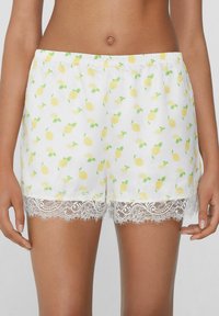 Witte shorts met een citroenprint in geel en groen, voorzien van een bloemenkant afwerking aan de zoom voor extra detail en textuur.