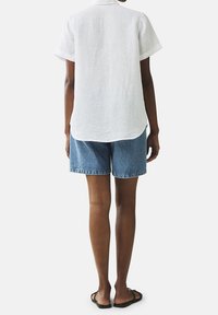 Camicia bianca di lino con maniche corte, abbinata a pantaloni shorts in denim blu. Il tessuto sembra leggero con una finitura strutturata. Design semplice.