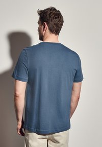 Modré bavlněné tričko s krátkým rukávem, klasickým kulatým výstřihem, hladkou texturou a volným střihem, zobrazené zezadu.