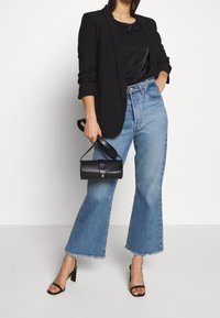 Sort blazer over en sort top, parret med højtaljede lysblå flared jeans. Holder en lille sort håndtaske. Sort strappy højhælede sko.