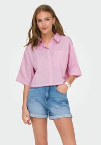 Lyserødstribet kortærmet skjorte med krave og lomme, parret med blå denim shorts med opfoldede ben. Enkel design, glat tekstur.
