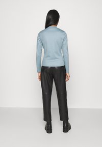 Maglia a maniche lunghe azzurro chiaro con scollatura texturizzata, abbinata a pantaloni in pelle nera a vita alta e stivali neri chunky.