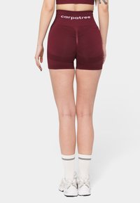 Pantalones cortos deportivos burdeos con una cinturilla alta que presenta el texto blanco "carpatree". Textura suave con un diseño ajustado, cortados por encima del muslo medio.