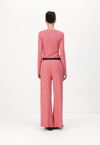 Red and white patterned long-sleeve top paired with high-waisted, wide-leg pants. Features a black waistband. Smooth, stretch fabric.