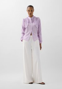 Lila overhemd met knoopsluiting en ruches, lange mouwen, gecombineerd met witte wijde broek. Glad textuur met subtiele strepen.