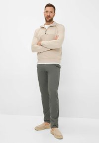 Light beige zip-up sweater with a high collar, paired with dark green pants and beige slip-on shoes, against a white background.