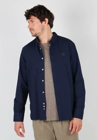 Chemise boutonnée bleu marine à manches longues, en tissu doux, avec des boutons blancs. Dotée d'un petit logo brodé sur la poitrine.