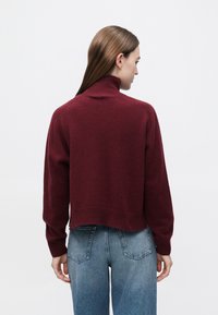 Bordowy sweter crop z wysokim kołnierzem i prążkowanym dołem. Miękka tekstura z długimi rękawami, zestawiony z jasnoniebieskimi, wysokim stanem jeansami.