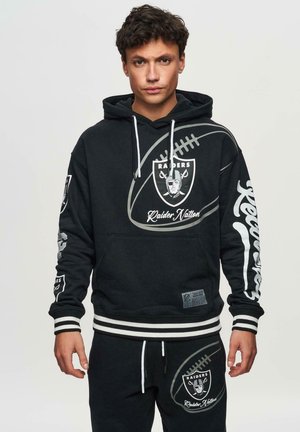 Hoodie noir avec un graphique de football et le logo "Raiders", accompagné de poignets et d'ourlet à rayures blanches. Pantalons noirs assortis avec un détail de logo.