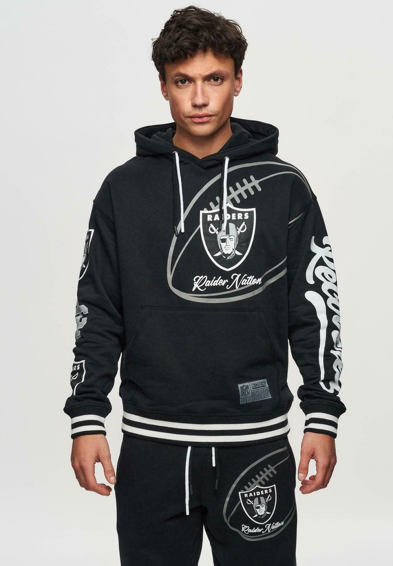 Mustapaita, jossa on jalkapallo-teema ja "Raiders" -logot, valkoisilla raidallisilla hihansuilla ja helmalla. Yhteensopivat mustat housut, joissa on logot yksityiskohtana.