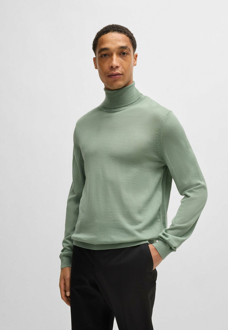 Light green turtleneck sweater in a soft, textured fabric. Fitted design with long sleeves and ribbed cuffs, paired with black trousers.