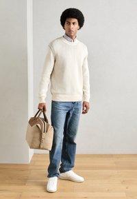 Suéter crema con cuello redondo, jeans azules, zapatillas blancas y un bolso beige con acentos marrones. Textura suave, diseño casual.