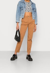 Giacca di jeans, top corto a strisce zebra in bianco e nero, pantaloni slim-fit marroni, borsa a tracolla nera intrecciata, scarpe con platform nere e lucide.