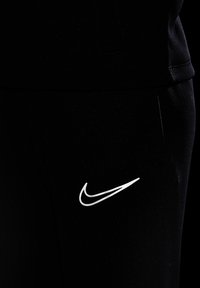 Schwarze Sporthose aus weicher Stoffqualität mit einem auffälligen weißen Nike-Swoosh-Logo auf der linken Seite, nahe der Tasche.