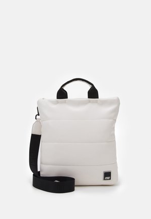 Sac à main carré matelassé blanc avec poignées noires et bandoulière noire réglable posé sur un fond uni.