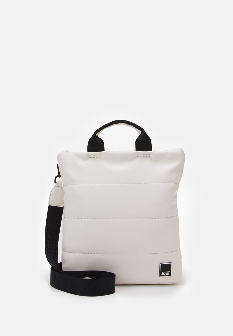 Sac à main carré matelassé blanc avec poignées noires et bandoulière noire réglable posé sur un fond uni.