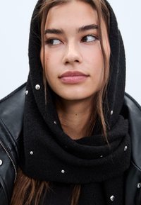 Sciarpa nera, morbida, con un tessuto testurizzato, caratterizzata da dettagli metallici. Indossata con una giacca di pelle nera.