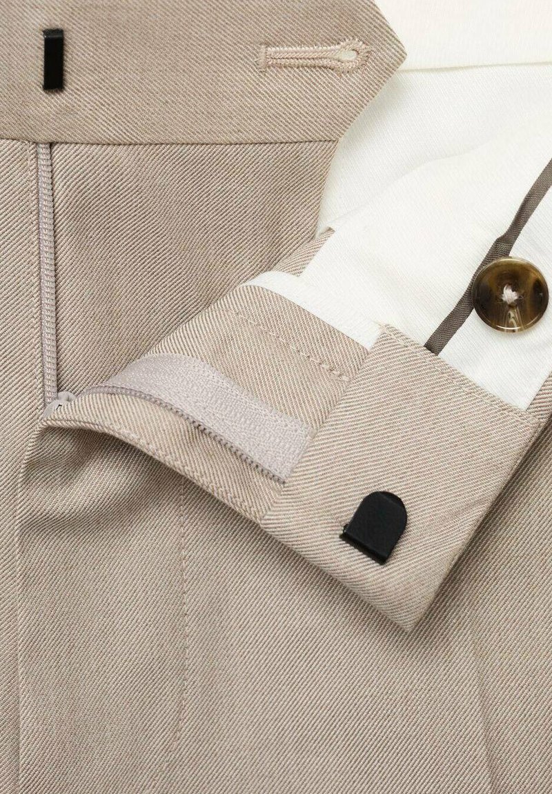 Beige skræddersyede bukser med slim fit, diagonalt stribet tekstur, sorte hardware-detaljer og hvid foer med en knapdetalje.