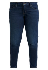 Jeans ajustados de color azul oscuro con bolsillos frontales, pasadores para cinturón y cierre de botón, exhibidos sobre un fondo blanco.
