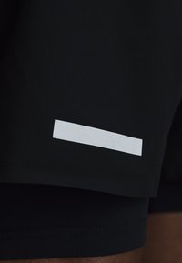 Μαύρο ύφασμα με μια μικρή οριζόντια αντανακλαστική λωρίδα κοντά στην άκρη, πιθανώς μέρος ρούχου ή αθλητικής ένδυσης.