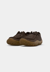 Zapatos de ante marrón con una forma redondeada, que cuentan con una suela de goma texturizada con pequeños relieves para mejorar el agarre y costuras decorativas a lo largo de los bordes.