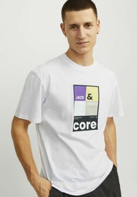 Balta medvilnės marškinėliai su grafiniu spausdiniu, kuriame pavaizduoti violetiniai, geltoni ir žali stačiakampiai, o juodu šriftu užrašyta "JACK & JONES core".